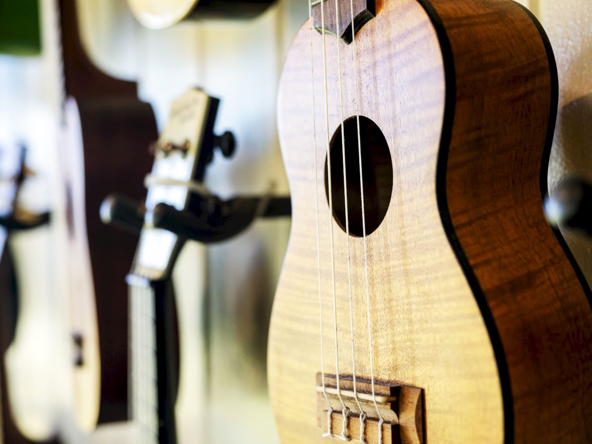 The image shows a close-up of a ukulele hanging on a wall, with other string instruments blurred in the background.