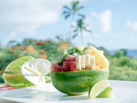 A half papaya filled with assorted fruits like bananas, kiwi, and watermelon, placed on a plate next to a lime wedge.