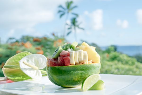 A half papaya filled with assorted fruits like bananas, kiwi, and watermelon, placed on a plate next to a lime wedge.