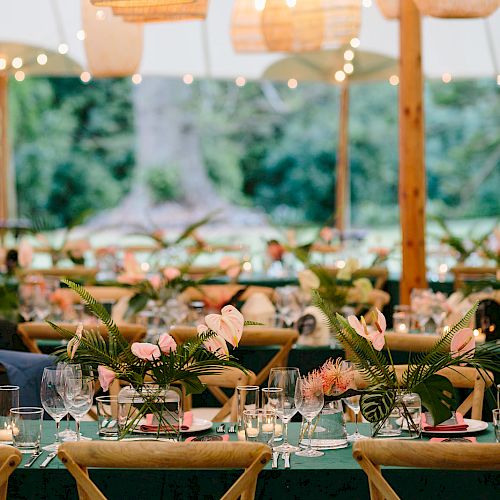 An outdoor dining setup with wicker pendant lights, floral centerpieces, string lights, and tableware, creating a festive and elegant atmosphere.