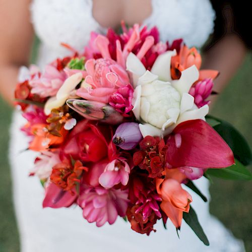 A person in a white lace dress holding a vibrant bouquet of red, pink, and white flowers.