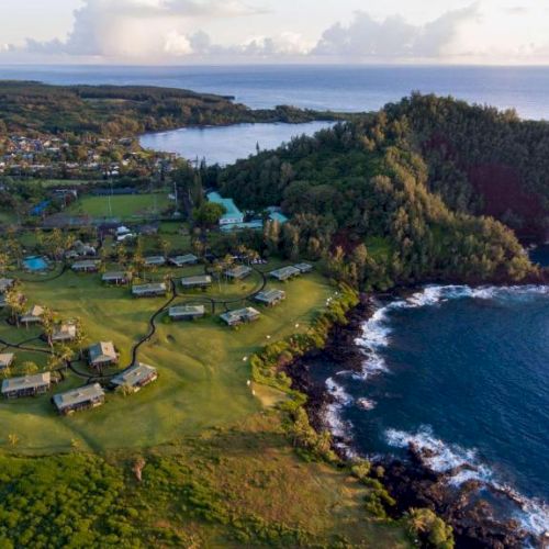 This image features a scenic coastal landscape with lush greenery, clustered buildings, rocky shorelines, and the ocean extending into the horizon.