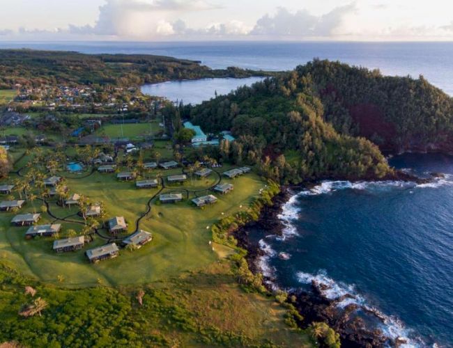 This image features a scenic coastal landscape with lush greenery, clustered buildings, rocky shorelines, and the ocean extending into the horizon.