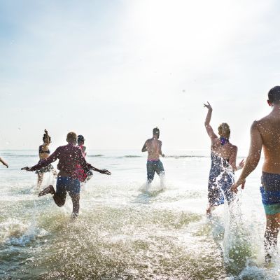 A group of people playing and splashing in the ocean on a sunny day, looking happy and carefree.