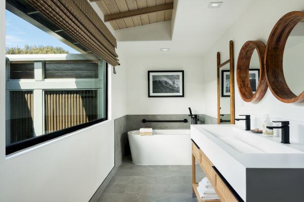 A modern bathroom with a bathtub, large mirrors, a double sink vanity, and a large window bringing in natural light.