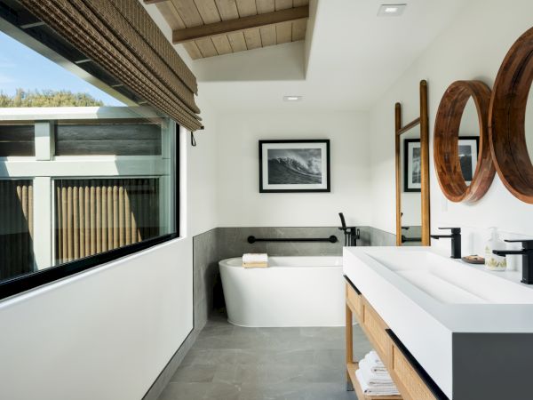 A modern bathroom with a bathtub, large mirrors, a double sink vanity, and a large window bringing in natural light.