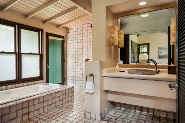 The image shows a bathroom with tiled floors and walls, a bathtub by the window, and a vanity with a sink and mirror.