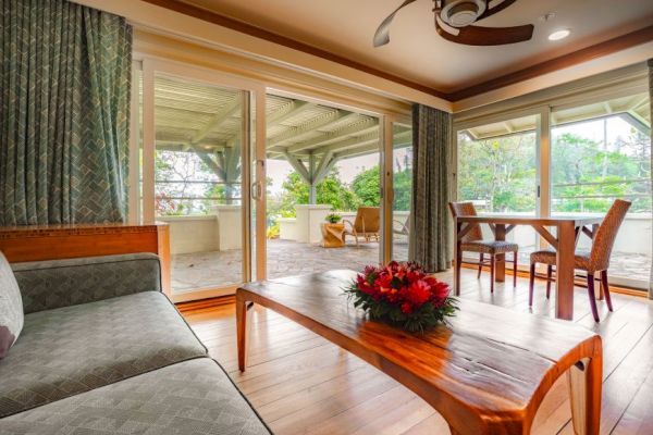 A cozy living room with wooden furniture, large windows, a ceiling fan, and a view of a spacious outdoor patio adorned with plants ends the sentence.