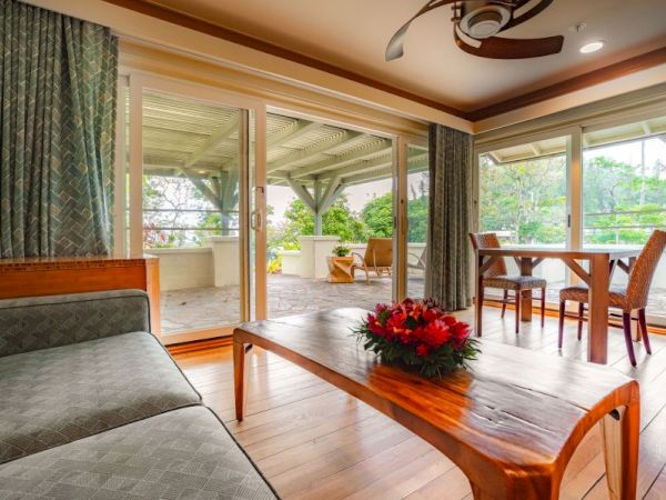 A cozy living room with wooden furniture, large windows, a ceiling fan, and a view of a spacious outdoor patio adorned with plants ends the sentence.
