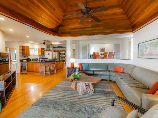 A spacious living room with a large sectional sofa, a rustic coffee table, an open kitchen, wooden ceiling, and modern furnishings.