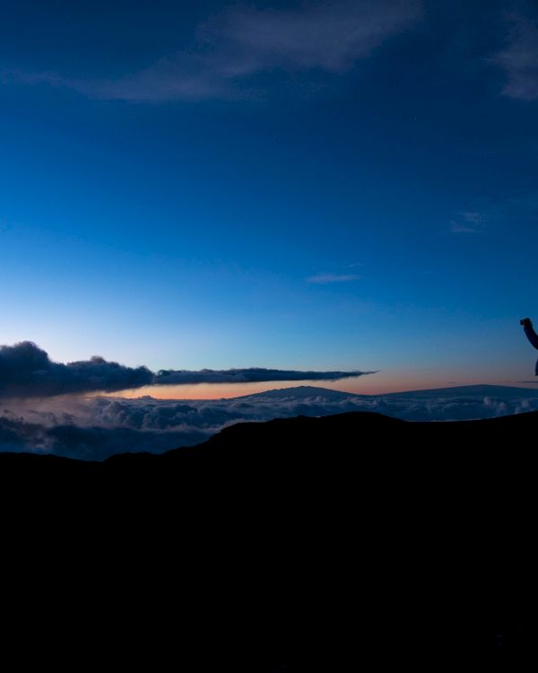 A silhouette of a person standing on a hill capturing the stunning twilight sky with scattered clouds and a subtle horizon in the background.