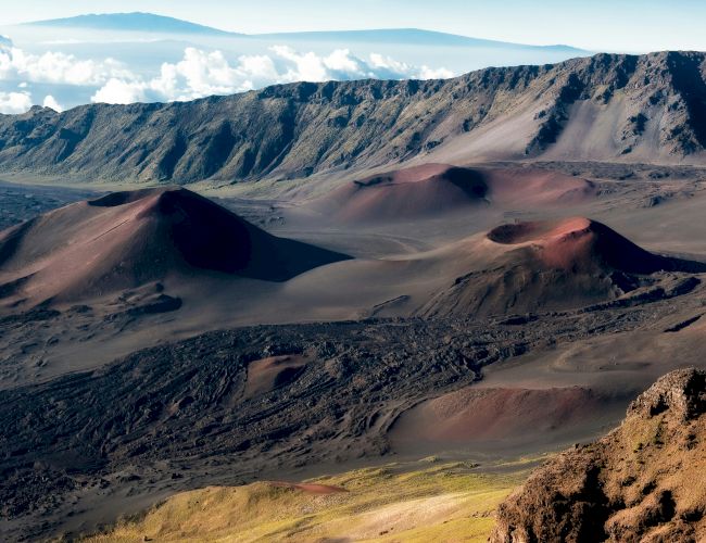 The image showcases a breathtaking volcanic landscape with rolling hills, crater peaks, and rugged terrains under a clear sky.