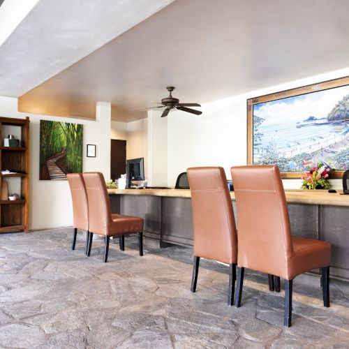 The image shows a reception area with brown chairs, computers, artwork on the wall, and a stone floor, creating a welcoming atmosphere.