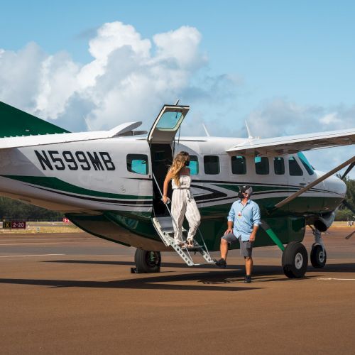 A green and white small aircraft on a runway with a person descending the stairs and another standing nearby, clear skies in the background.