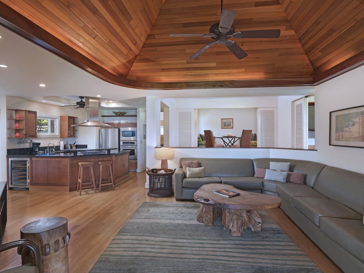 A spacious living room with a large sectional sofa, wooden ceiling, modern kitchen, and a rustic coffee table.