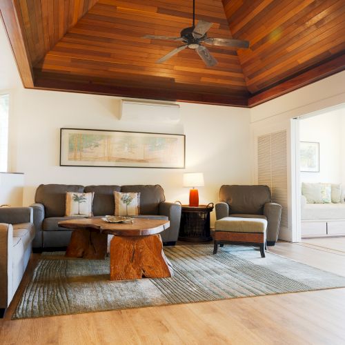 A spacious living room with wooden ceiling, cozy furniture, a large rug, and soft lighting. Earth tones and natural textures create warmth.