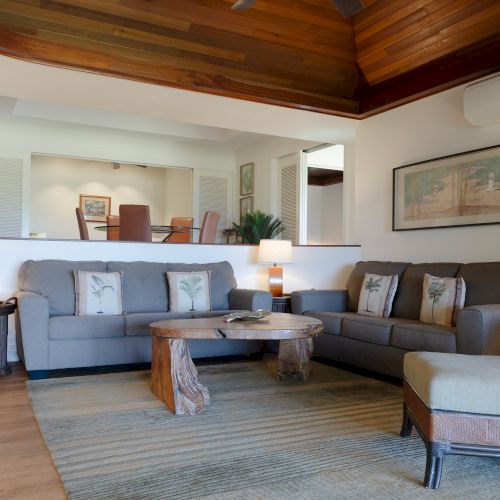 The image shows a cozy living room with gray sofas, a wooden coffee table, and warm lamps. A painting hangs on the wall, adding decor.