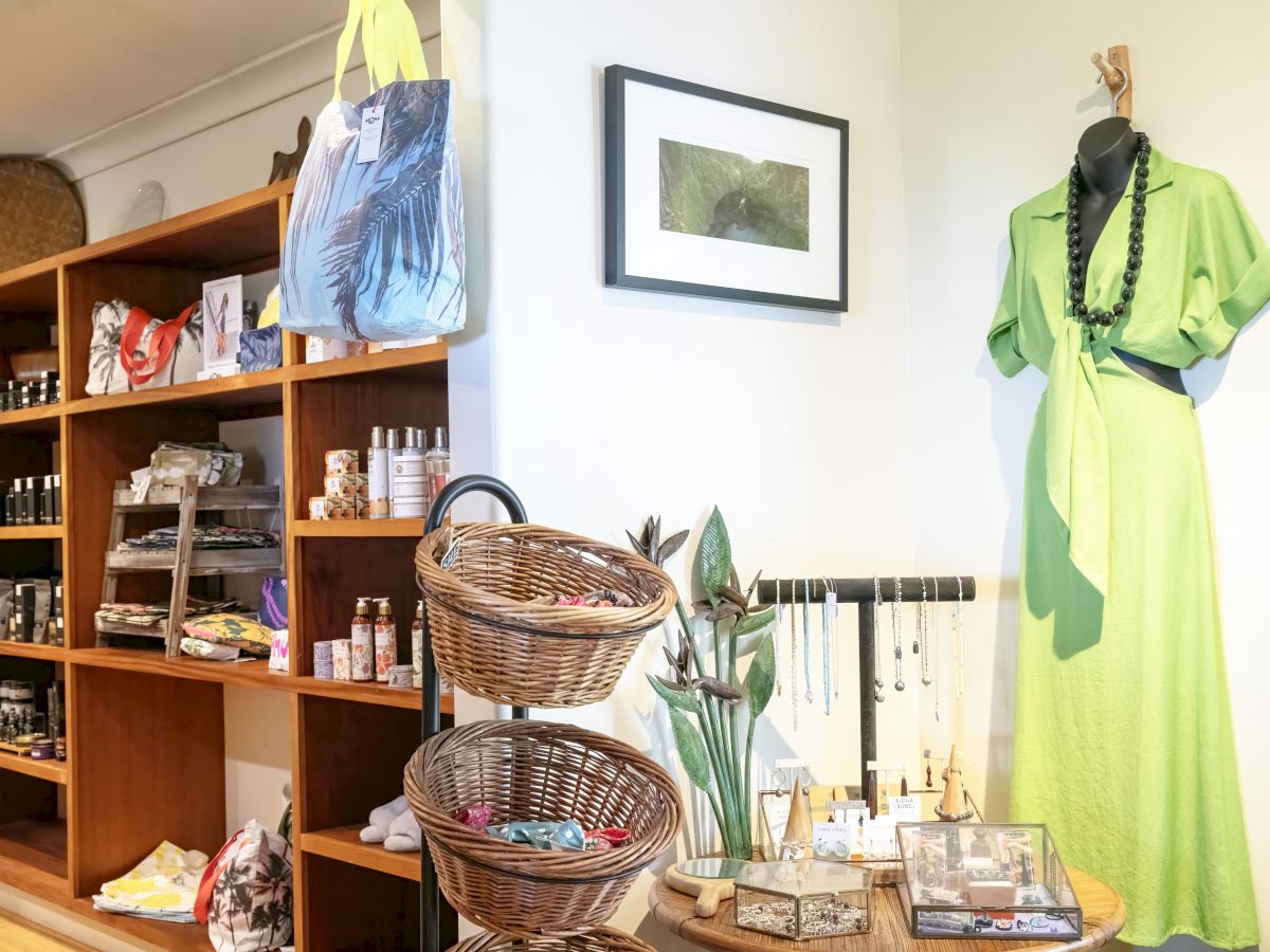 A shop interior with shelves of products, wicker baskets, a mannequin in a green dress, and jewelry displayed on a table.