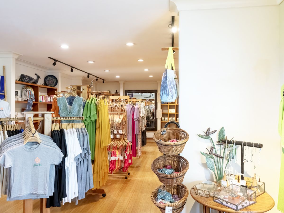 A clothing store interior with racks of colorful garments, baskets, and a jewelry display on a table in the foreground.