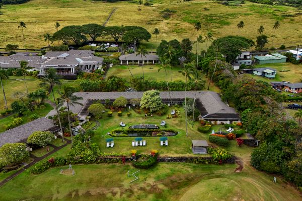Aerial view of a lush landscape featuring several buildings, gardens, and open green spaces surrounded by trees and fields.