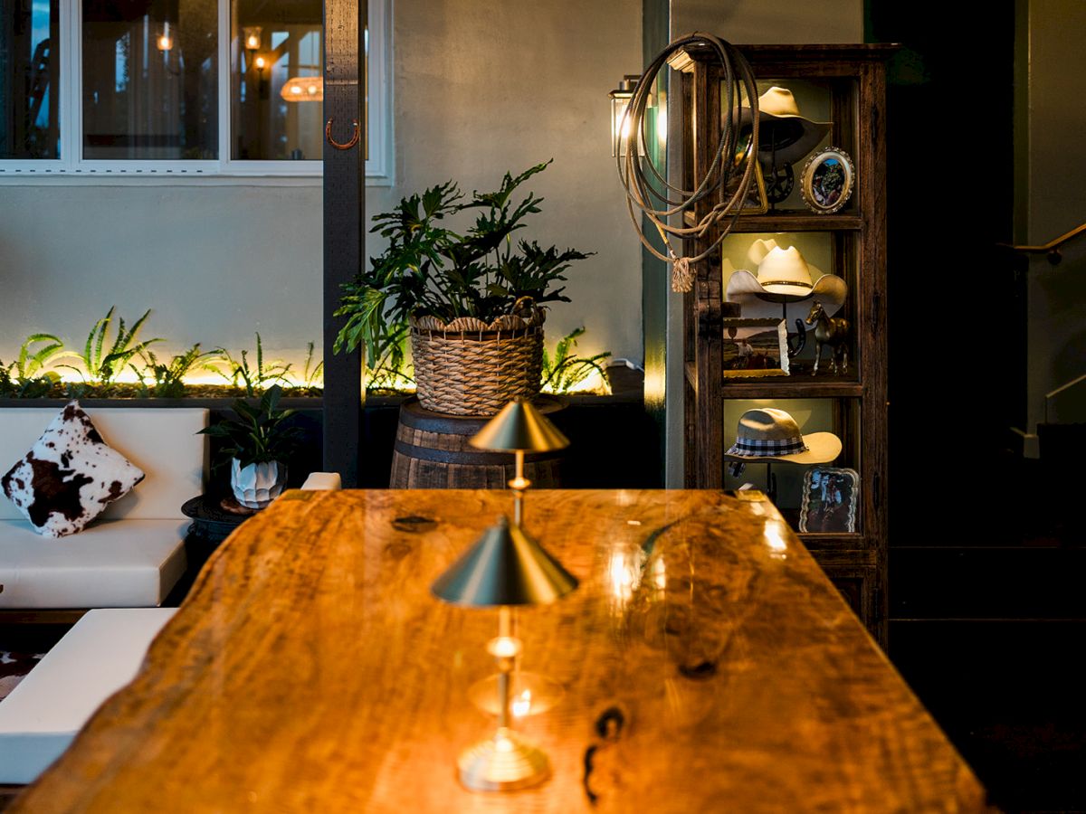 A cozy caf&eacute; patio at dusk with a wooden table, glowing lights, plants, and a shelf of cowboy hats and decor.