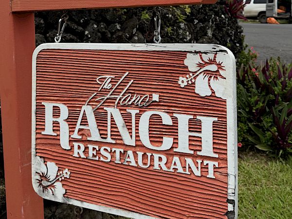 Two cold drinks in clear cups sit on a red &ldquo;Rainwater&rdquo; bar sign outdoors under a cloudy sky.