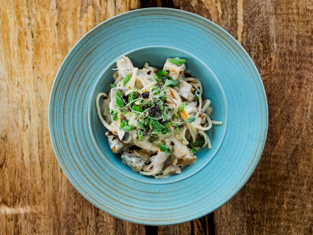 A bowl of creamy pasta with chunks of mushroom, green herbs, and microgreens on a blue plate.
