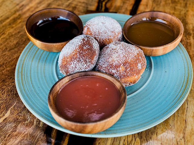 Powdered-sugar donuts served on a blue plate with three dipping sauces in small bowls.