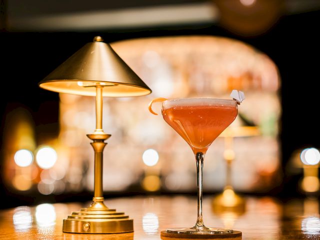 Warm bar scene with a martini cocktail on a table and a glowing lamp behind it.