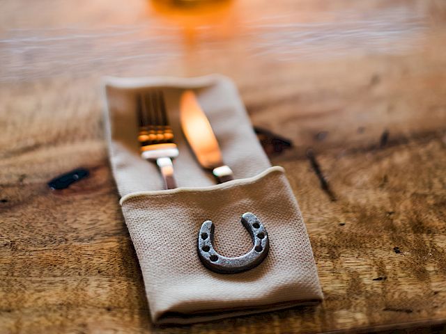 A lit lamp glows over a wooden table as a horseshoe charm rests on a folded cloth near scattered items.